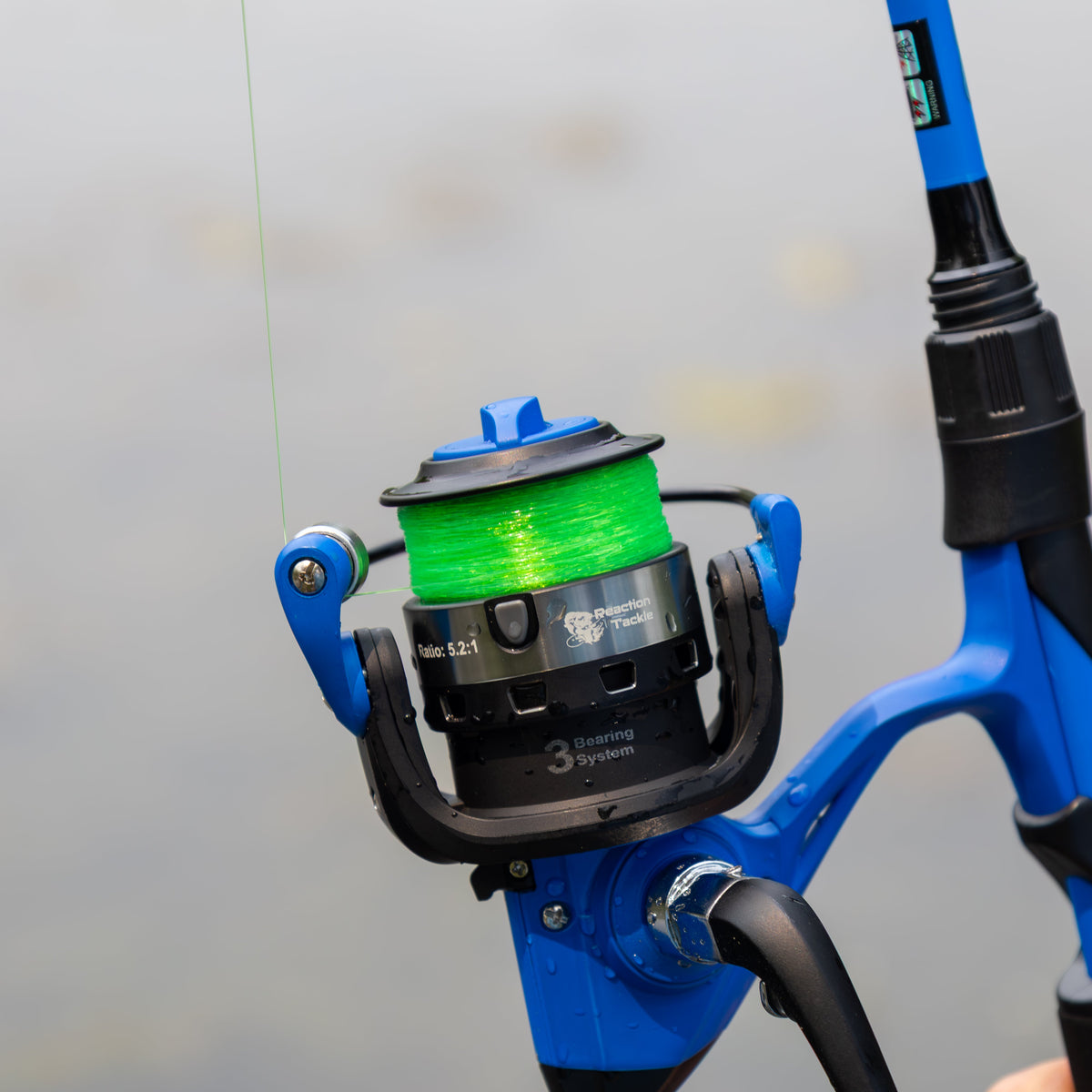 Close-up of a blue fishing rod with a green spool against a gray background